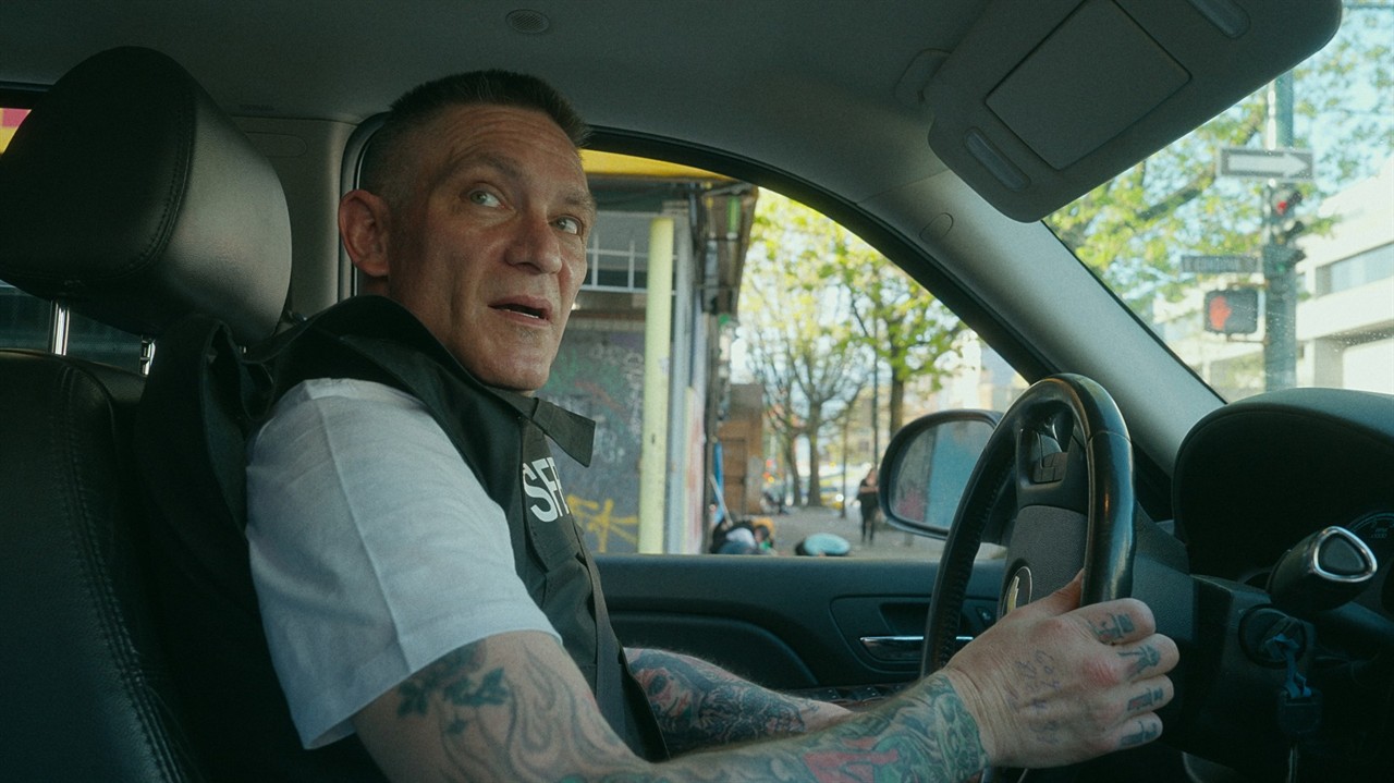 Man with buzz cut and tattoed arms driving